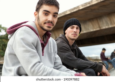 Side Portrait Of Two Attractive Latino Teenagers Friends Sitting Together And Relaxing Having A Break At An Urban Park During A Weekend Day, Outdoors. Active Young People Portrait And Lifestyle.