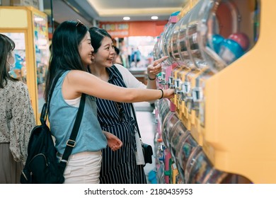 Side Portrait Two Happy Asian Girls Shopping Together Are Pointing And Looking At The Toys Gashapon While Having Fun With The Capsule Vending Machine In A Store.