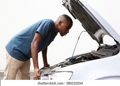 Side portrait of young african american guy looking under the hood of broken down car