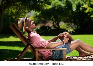 Side portrait of young african guy sitting on chair and listening to music outdoors - Powered by Shutterstock