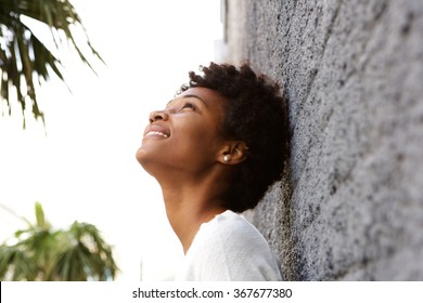 Side Portrait Of Young African Woman Leaning To A Wall Outside And Looking Up