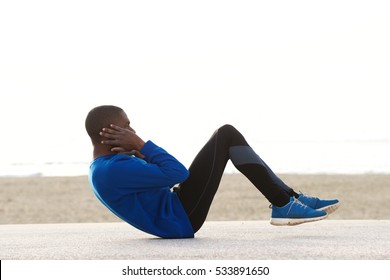 Side Portrait Of A Young Black Man Exercising On The Beach Doing Sit Ups