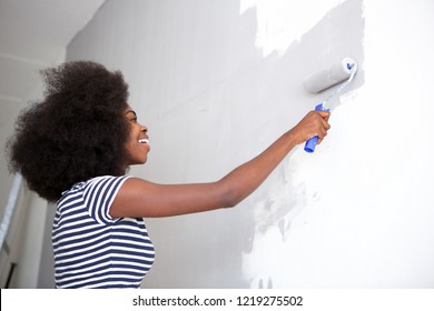 Side Portrait Of Young Black Woman Painting Wall At Home
