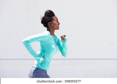 Side Portrait Of Young Black Woman Running Outside With Earphones