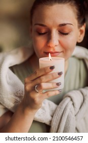 Side portrait of young calm woman holding lit candle in hands, closing eyes bringing close to her face and inhaling its aroma, smelling familiar scent while enjoying happy moment of comfort - Shutterstock ID 2100546457