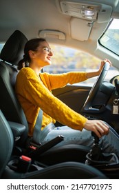 Side portrait of young caucasian woman driving car in the city with one hand on steering wheel and another on gear lever - Shutterstock ID 2147701975