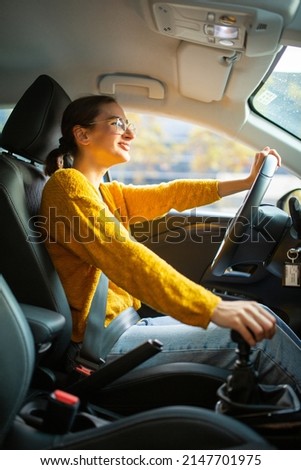 Side portrait of young caucasian woman driving car in the city with one hand on steering wheel and another on gear lever
