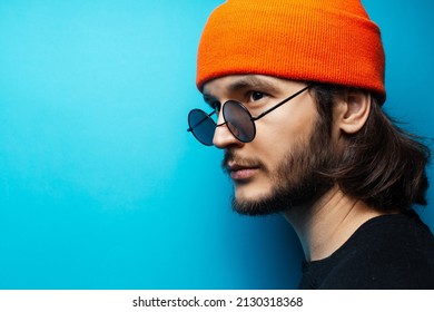 Side Portrait Of Young Man On  Blue Background. Wearing Sunglasses And Hat.