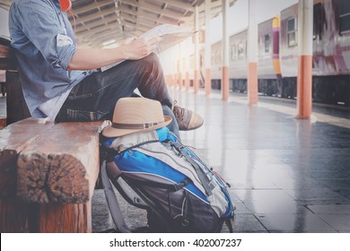 Side Portrait Of A  Young Man Traveler Sitting With Map Choose Where To Travel And Bag Waiting For Train At Train Station, Vintage Tone Filter Effected