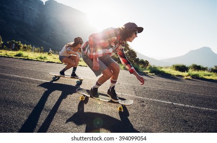Side portrait of young people skateboarding together on road. Young man and woman longboarding down the road on a sunny day.