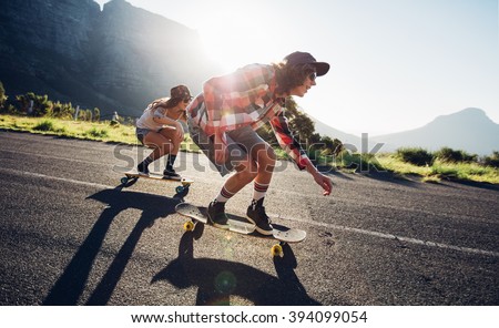 Side portrait of young people skateboarding together on road. Young man and woman longboarding down the road on a sunny day.