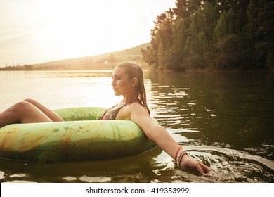 Side Portrait Of Young Woman In Lake On Inflatable Ring. Woman Relaxing In Water On A Summer Day.