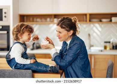 Side Profile Of An Adult Mother Trying To Feed Her Child While He's Eating Banana Bread.