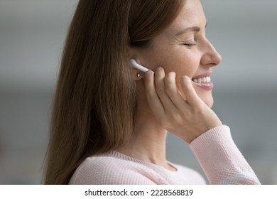 Side profile close up face view peaceful pretty woman enjoy song through wireless earphones stand indoors smile relish classical music with eyes closed. Hobby, weekend leisure using modern tech, mood