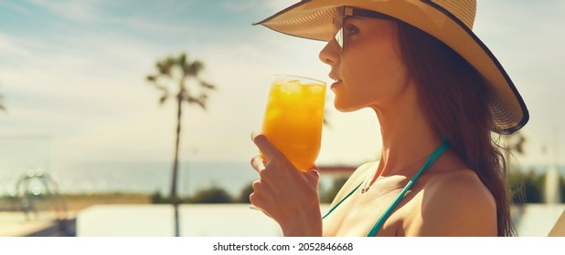 Side Profile Cropped Panoramic View Face Beautiful Woman, Wear Straw Hat Hold Glass Drinks Orange Juice Or Cocktail Refreshing At Hot Day Relax On Deckchair Near Pool. Enjoy Summer Holidays Concept