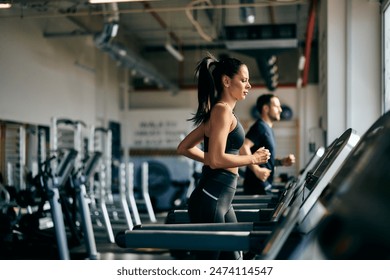 Side profile of a fit girl running on a treadmill at the gym.