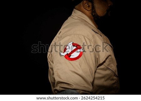 Side profile of a Ghostbusters cosplayer with the iconic Ghostbusters logo clearly visible on the uniform. A nostalgic tribute to the classic paranormal comedy franchise.