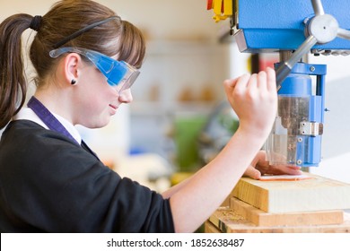 A Side Profile Of A Girl Using A Drill To Cut Wood In A School Workshop While Wear Safety Goggles For Protection