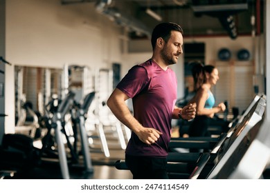 Side profile of a male and female running on a treadmill at the gym, focus on the man. - Powered by Shutterstock