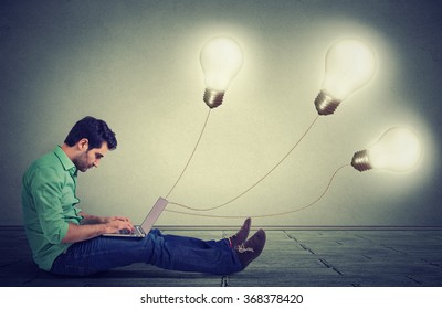 Side Profile Man Sitting On Floor Using A Laptop With Many Light Bulbs Plugged In It