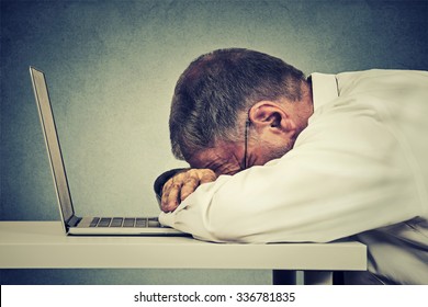 Side profile mature business man sleeping on a laptop isolated on grey office wall background. Sleep deprivation, long working hours concept