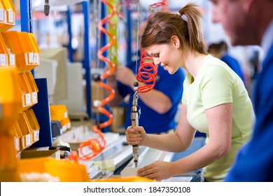 A side profile medium shot of a happy young female worker in casuals operating machinery on a production line in a factory.