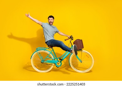 Side profile photo of funky crazy excited man wear gray t-shirt denim jeans sitting new retro bicycle raise palm hello friends isolated on yellow color background - Shutterstock ID 2225251403