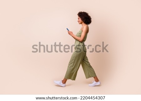 Side profile photo of gorgeous positive cheerful girl curly hairstyle wear khaki overall walk chatting isolated on beige color background