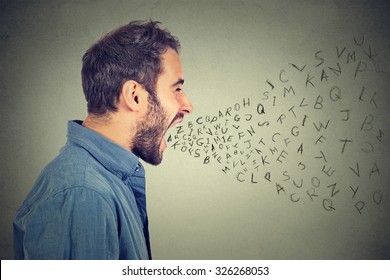 Side Profile Portrait Of Young Angry Man Screaming With Alphabet Letters Flying Out Of Wide Open Mouth Isolated On Gray Wall Background 