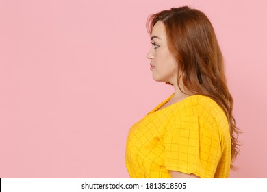 Side profile view of attractive beautiful pretty young redhead plus size body positive woman 20s in yellow dress posing looking aside isolated on pastel pink color wall background studio portrait