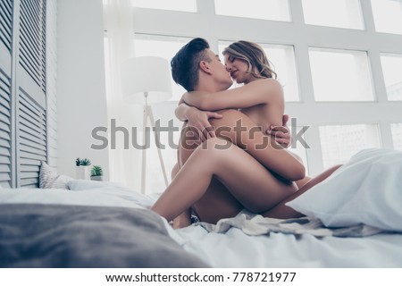 Side profile view of  brunet macho and beautiful blonde prostitute, almost naked, sit in bed on bedclothes, linens, embracing, she is on top, sensual, intense, white loft room