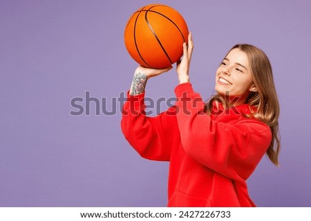 Side profile view happy young fun woman fan she wearing red hoody cheer up support basketball sport team hold in hand shoot ball look camera isolated on plain purple background. Sport leisure concept