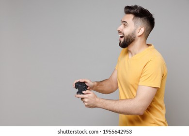 Side Profile View On Young Caucasian Smiling Bearded Happy Excited Student Gamer Man 20s Winner Yellow Basic T-shirt Play Pc Game With Joystick Console Isolated On Grey Background Studio Portrait