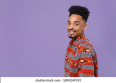 Side profile view of smiling young african american man in casual colorful shirt posing look camera isolated on violet background studio portrait. People emotions lifestyle concept. Mock up copy space