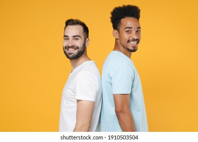 Side profile view of smiling young two friends european african american men 20s wearing white blue casual t-shirts standing looking camera isolated on bright yellow colour background studio portrait - Shutterstock ID 1910503504