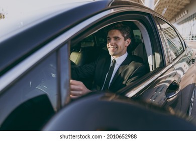 Side Profile View Smiling Young Driver Smiling Businessman Man 20s Wear Black Dinner Suit Driving Car Taxi Hold Steering Wheel Look Camera Vehicle Transport Traffic Lifestyle Business Trip Concept