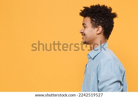Side profile view smiling young man of African American ethnicity he wear casual blue shirt look aside isolated on yellow background studio portrait. People sincere emotions lifestyle concept. Mock up