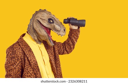 Side profile view studio portrait of happy funny curious excited man in dinosaur mask and leopard costume jacket standing isolated on yellow background, holding binoculars and looking in distance - Shutterstock ID 2326308211