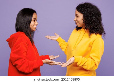 Side profile view two fun young little kid teen girls women they wear red yellow hoodie casual clothes talk to each other chit chat isolated on plain pastel light purple background. Lifestyle concept