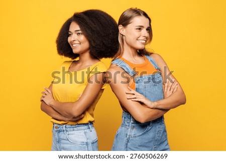 Side profile view two young friends buddies women they wear denim casual clothes hold hands crossed folded together smile isolated on plain yellow orange background studio portrait. Lifestyle concept