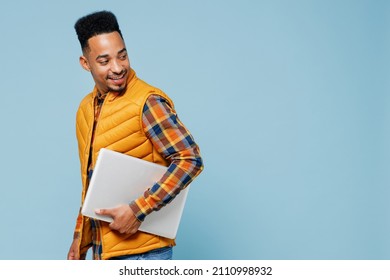 Side profile view young black man 20s years old wears yellow waistcoat shirt hold use work on laptop pc computer walking looking behind isolated on plain pastel light blue background studio portrait