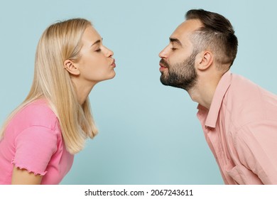 Side profile view young couple two friends family man woman in casual clothes kiss each other with closed eyes while standing face to face together isolated on plain light blue color background studio
