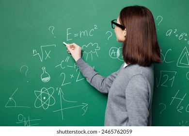 Side profile view young smart teacher woman wear grey casual shirt glasses write formula on board isolated on green wall chalk blackboard background studio. Education in high school college concept - Powered by Shutterstock