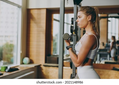 Side profile view young strong skinny sporty athletic sportswoman woman 20s wearing white sportswear warm up training do dummbells exercises in gym indoor Workout sport motivation lifestyle concept