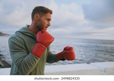 Side profile view young strong sporty athletic toned fit sportsman man in sports clothes red gloves boxing warm up training at sunrise sun dawn over sea beach outdoor on seaside in summer day morning - Powered by Shutterstock