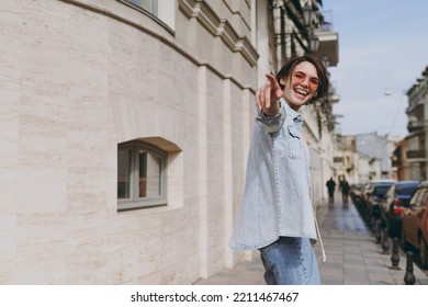 Side Profile View Young Tourist Excited Caucasian Woman 20s In Jeans Clothes Eyeglasses Walk In City Center Street Near Building Point Index Finger Aside. People Urban Youth Travel Lifestyle Concept.