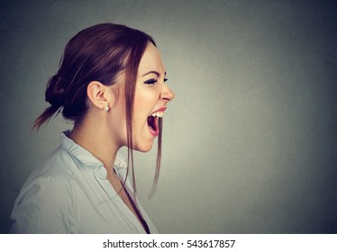 Side Profile Of Young Angry Woman Screaming With Wide Open Mouth Isolated On Gray Wall Background