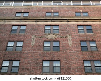 Side of Red Brick building with classical emblem featuring sets of two windows going upward