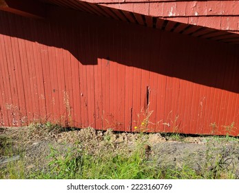 The side of a red building with paint missing and cracks in the wood.