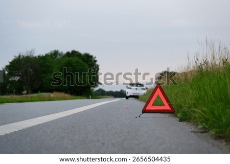 At the side of the road is a warning triangle, behind it a white car with a breakdown